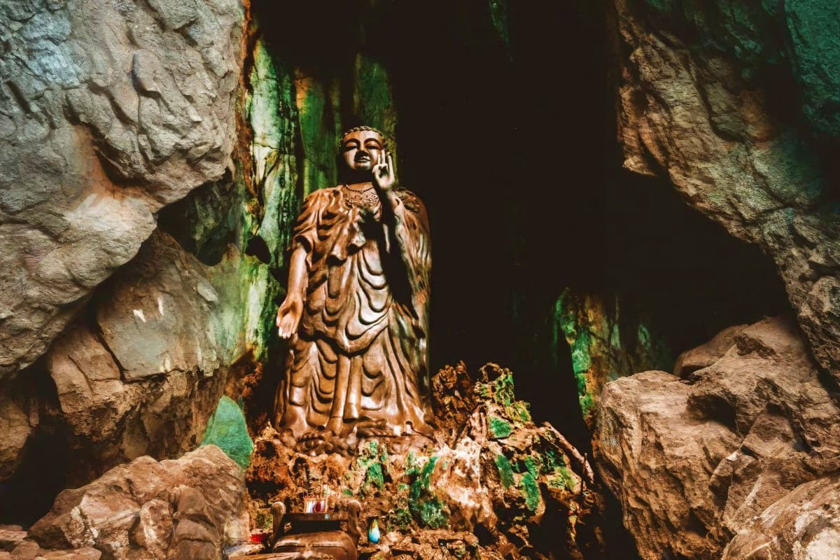 Golden Buddha statue inside cave surrounded by moss-covered stone walls at Marble Mountains