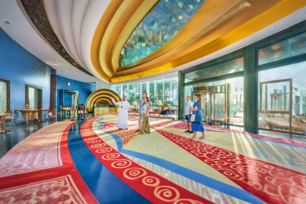 Luxurious interior hallway of Burj Al Arab with curved gold ceiling, blue walls, decorative patterned carpeting, and visitors