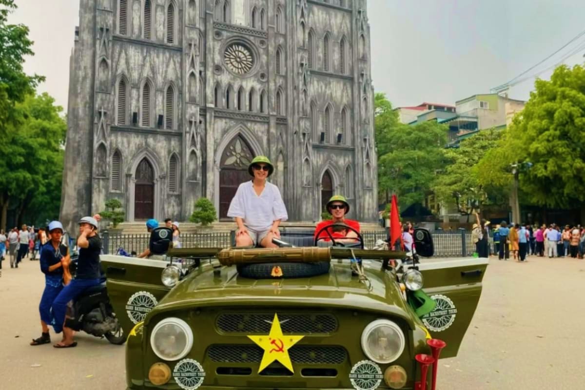 Tourists on military jeep with yellow star emblem posing in front of St. Joseph's Cathedral in Hanoi, Vietnam