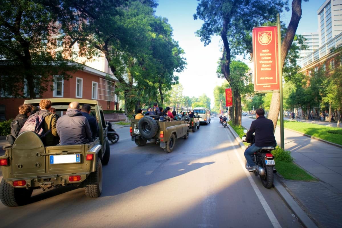 Tourists riding in open-air military jeeps on a tree-lined street during a guided city tour, with colonial buildings and a re