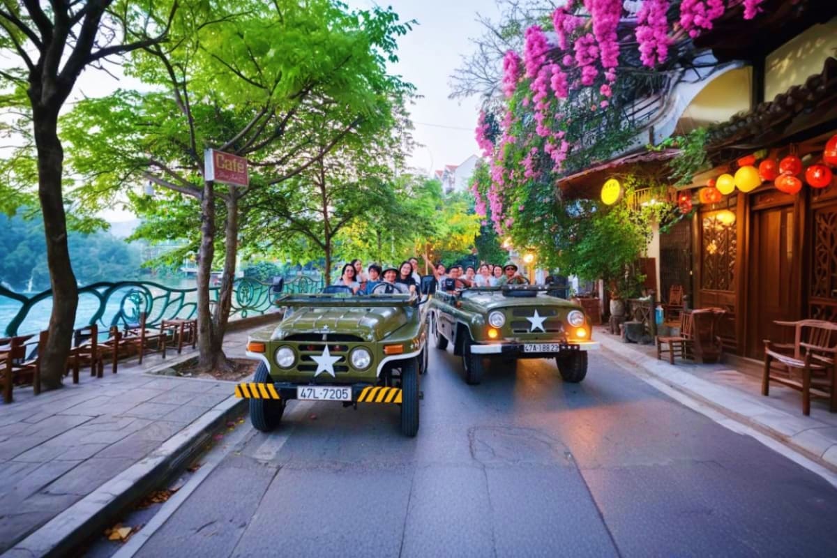 Vintage military jeeps carrying tourists driving through a scenic town street lined with pink bougainvillea flowers and green