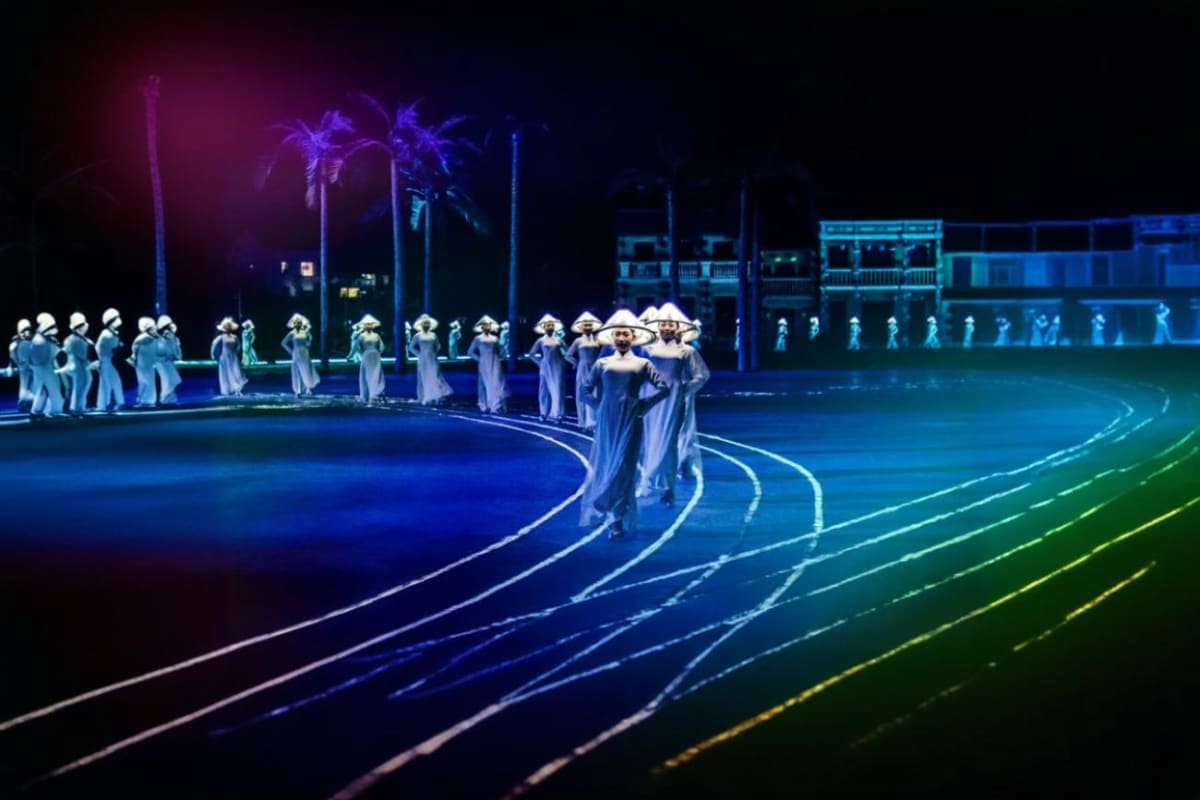 Large group of performers in white áo dài and conical hats arranged in geometric patterns on stage with colorful neon lightin