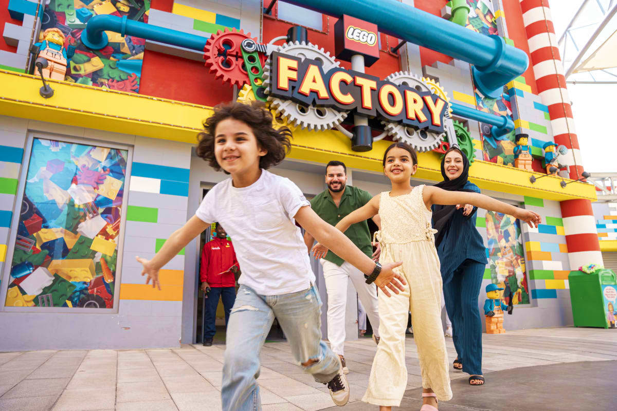 Family running outside LEGO Factory building at Legoland Dubai with colorful brick facade and large gear sign