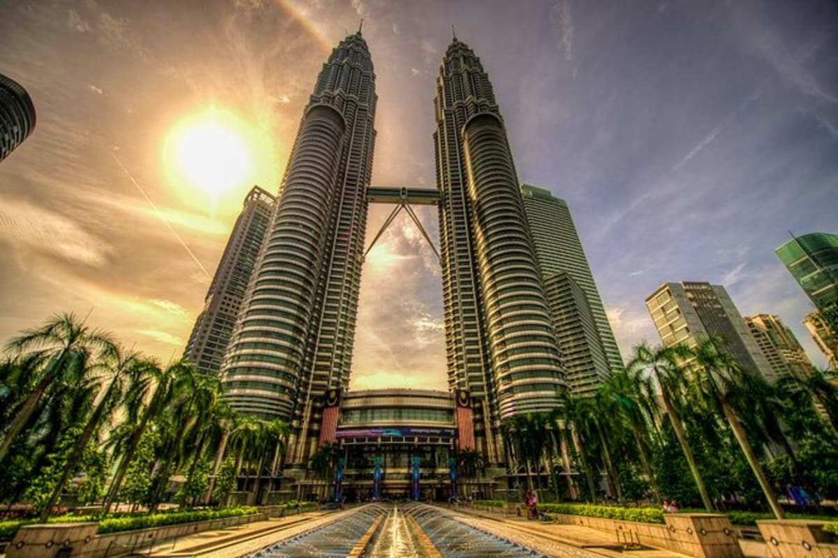 Petronas Twin Towers in Kuala Lumpur with symmetrical skyscrapers, connecting bridge, palm trees, and sunset sky