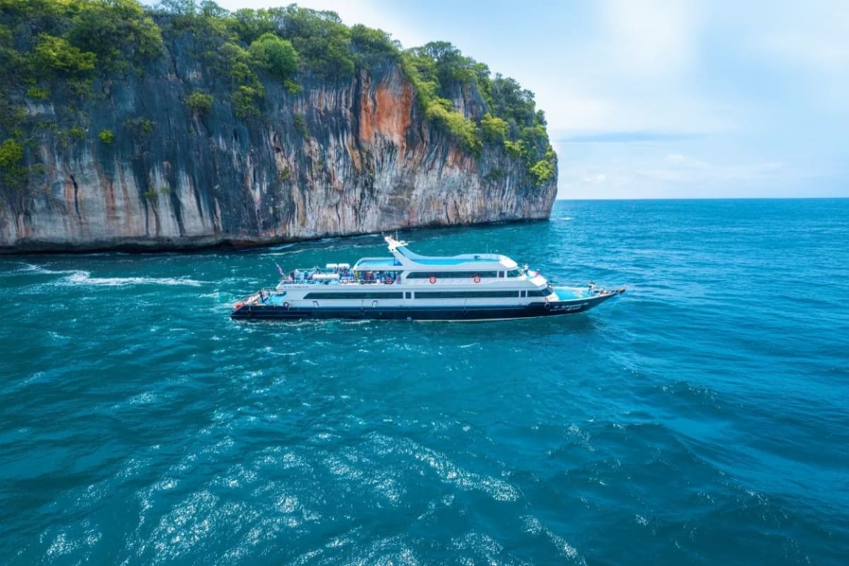 White and blue passenger ferry boat anchored in turquoise waters near tall limestone cliff formations in tropical sea