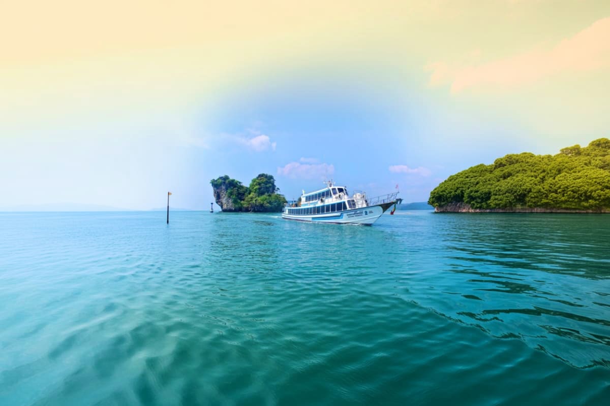 White and blue ferry boat anchored in turquoise tropical waters with limestone islands and green vegetation under blue sky