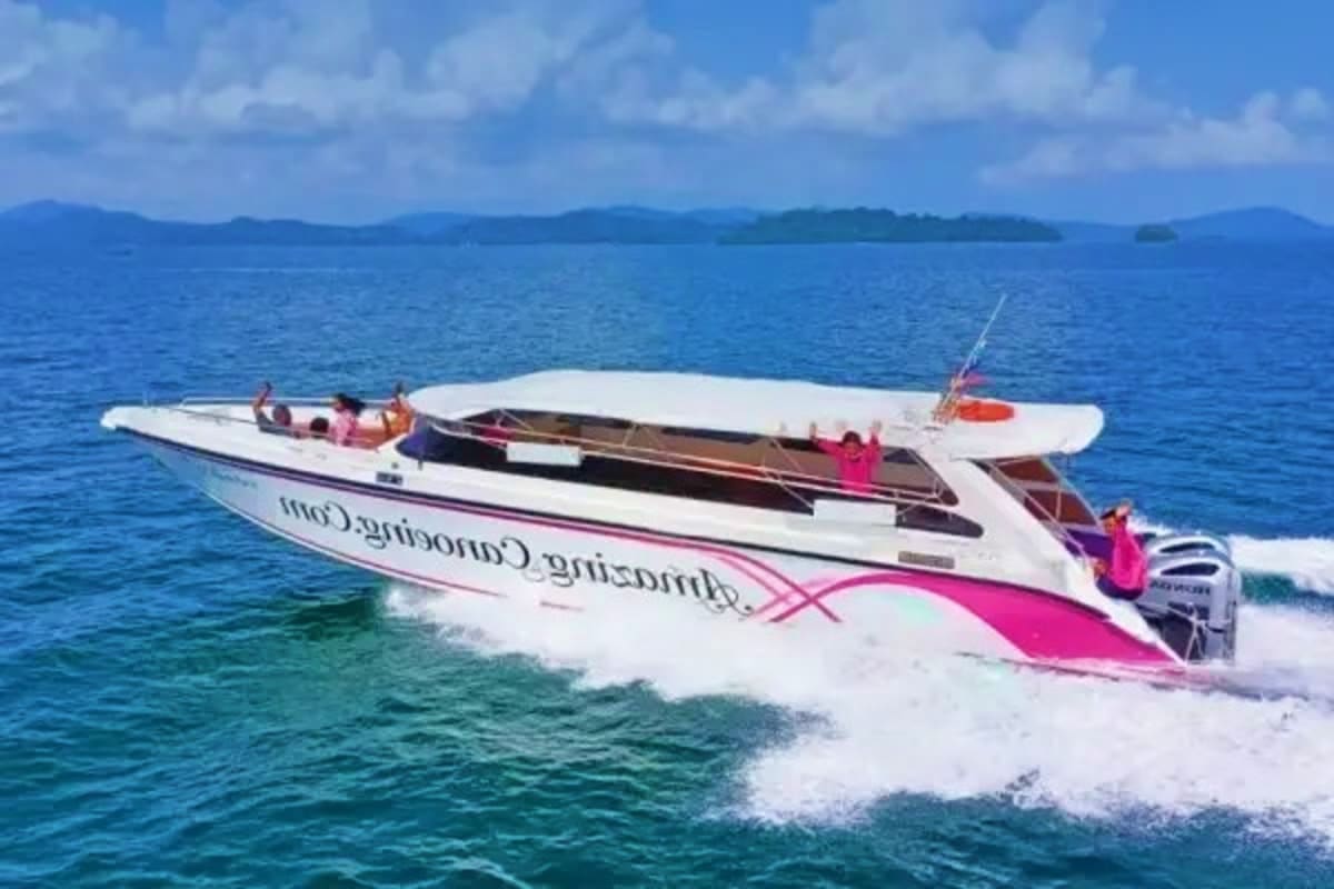 White and pink speedboat with passengers anchored in shallow turquoise water near tropical islands under blue sky