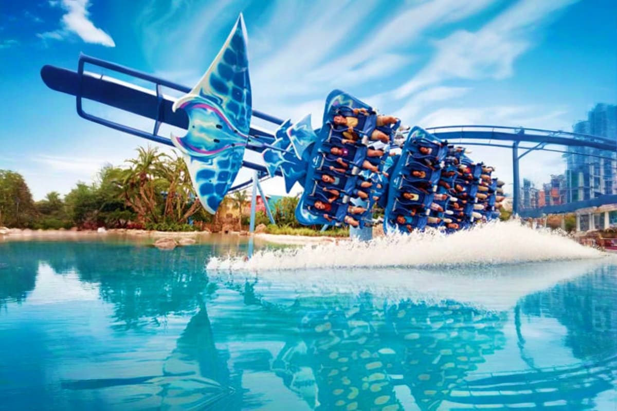 Blue roller coaster with manta ray-shaped ride vehicles over turquoise water at SeaWorld Abu Dhabi theme park