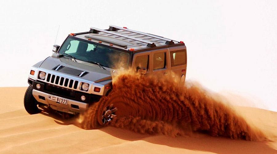 Hummer Desert Safari Abu Dhabi Hummer SUV kicking up dust while driving across sand dunes in Abu Dhabi desert