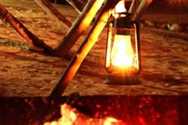 Lit lantern hanging from wooden pole above glowing campfire in desert night setting