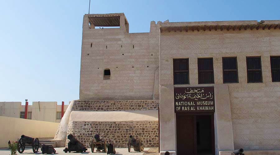 National Museum of Ras Al Khaimah with traditional stone fortification tower and entrance signage under clear blue sky