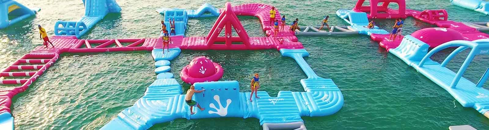 Aqua Fun Dubai Inflatable water park with pink and blue obstacle course structures in Dubai sea, people enjoying water activities and games