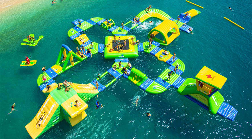 Aqua Fun Dubai Aerial view of colorful inflatable water park with green and yellow structures, slides, and swimmers in turquoise water