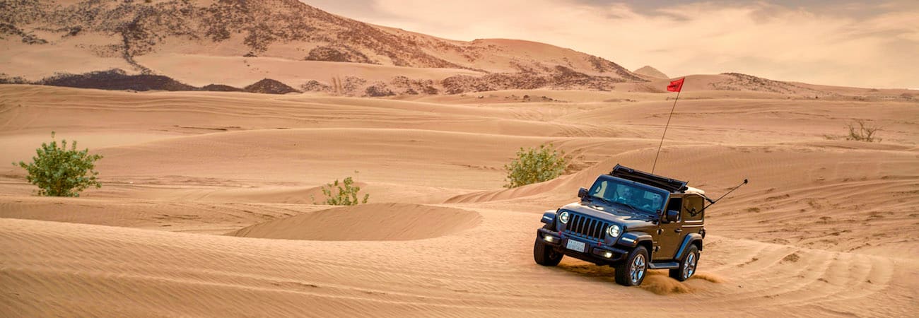 Jeddah VIP Desert Safari Jeep with red flag parked on sand dunes in desert landscape with scattered vegetation and mountains in background