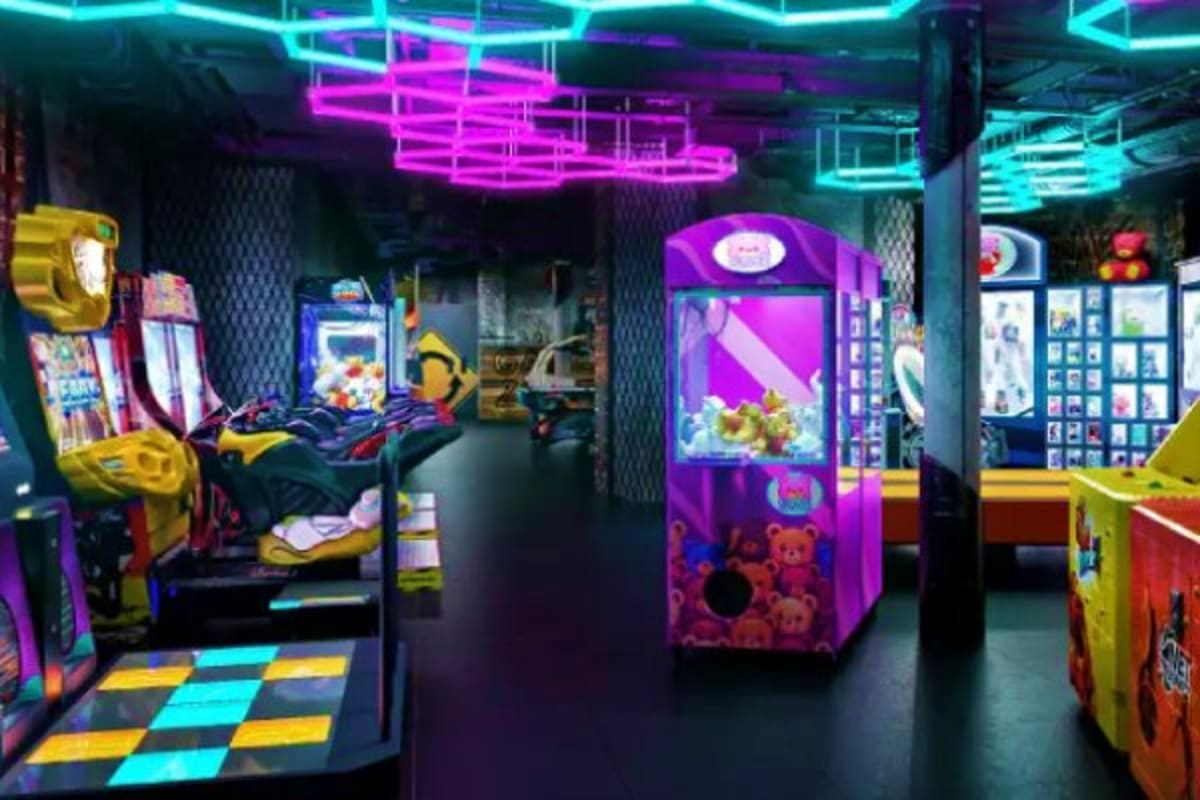 Modern arcade game room with neon cyan and magenta lighting, colorful gaming machines, and checkered floor on a cruise ship.