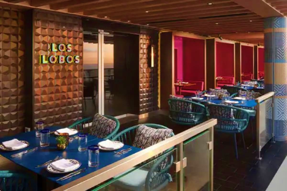 Los Lobos restaurant interior with blue dining table, place settings, and magenta accent walls on Norwegian Cruise Line ship