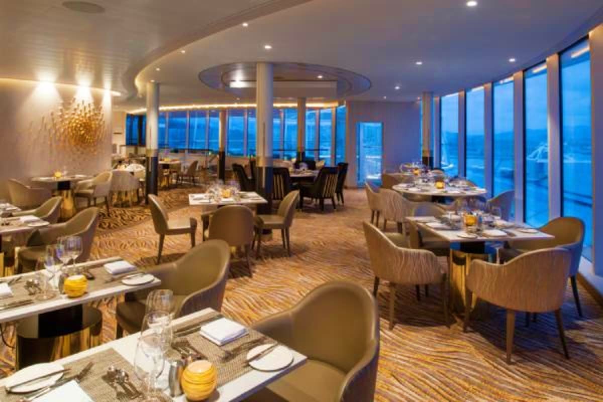 Upscale dining room on Spectrum of the Seas with floor-to-ceiling windows overlooking ocean at dusk, elegant place settings a