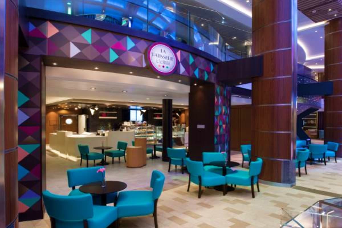 Modern cruise ship lounge area with turquoise seating, geometric patterned walls, and Baesler's cafe storefront with neon sig
