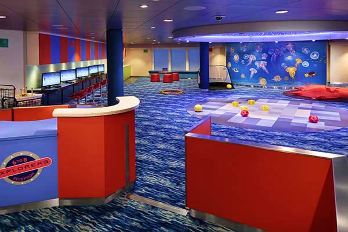 Kids' play area on Spectrum of the Seas with interactive games, blue ocean-themed walls, red furniture, and activity stations