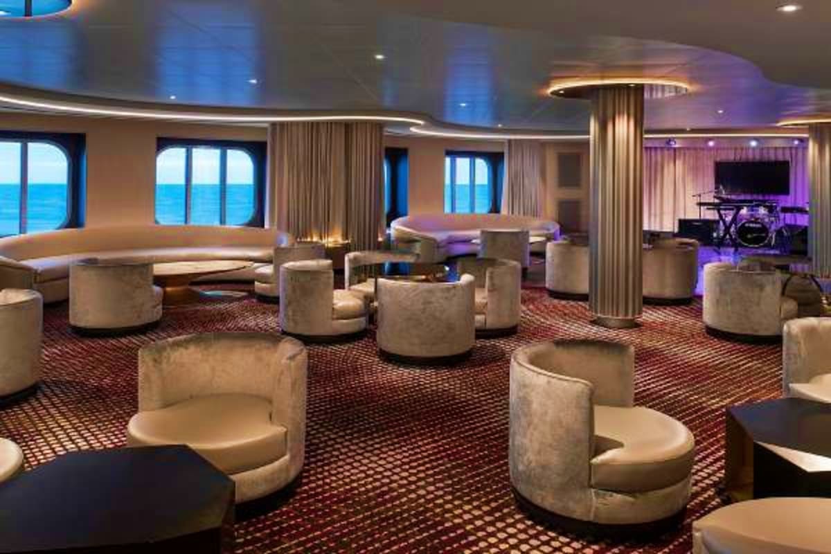 Modern cruise ship lounge with curved seating, ocean views through large windows, purple accent lighting, and a piano in the 