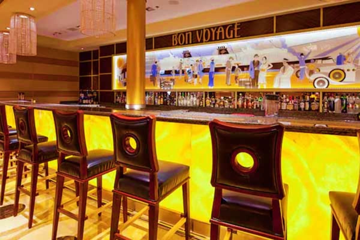 Bon Voyage lounge bar on Disney Fantasy cruise ship with illuminated yellow panels, bar stools, and mural of passengers in ba