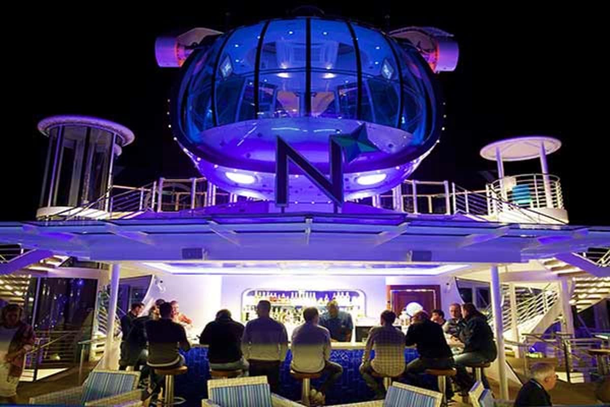Passengers gathered on cruise ship deck at night with illuminated spherical observation pod and blue-purple ambient lighting 