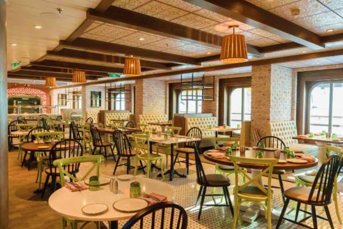 Modern restaurant dining room with round and oval tables, black Windsor chairs, yellow upholstered booths, exposed brick wall