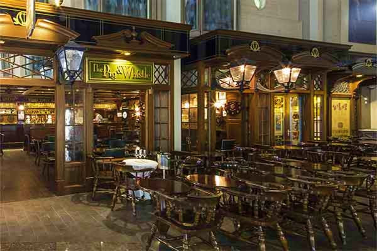 The Pig and Whistle pub storefront with wooden facade, brass lighting fixtures, and outdoor seating area on a cruise ship pro