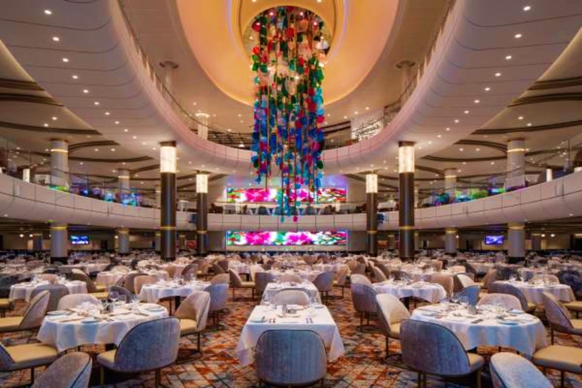 Grand dining room on Independence of the Seas cruise ship with round tables, colorful floral chandelier installation, and mul