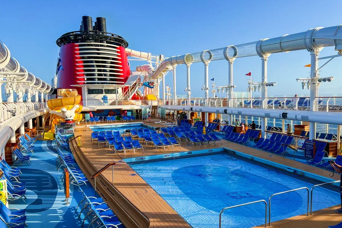 Four Nights Singapore and Langkawi Escape Cruise ship pool deck with blue lounge chairs, swimming pool, red funnel smokestack, and white piping under clear sky