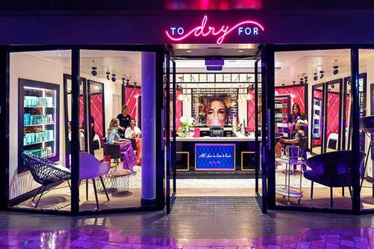 Modern beauty salon storefront with pink neon signage, purple accents, glass doors, and customers inside receiving salon serv
