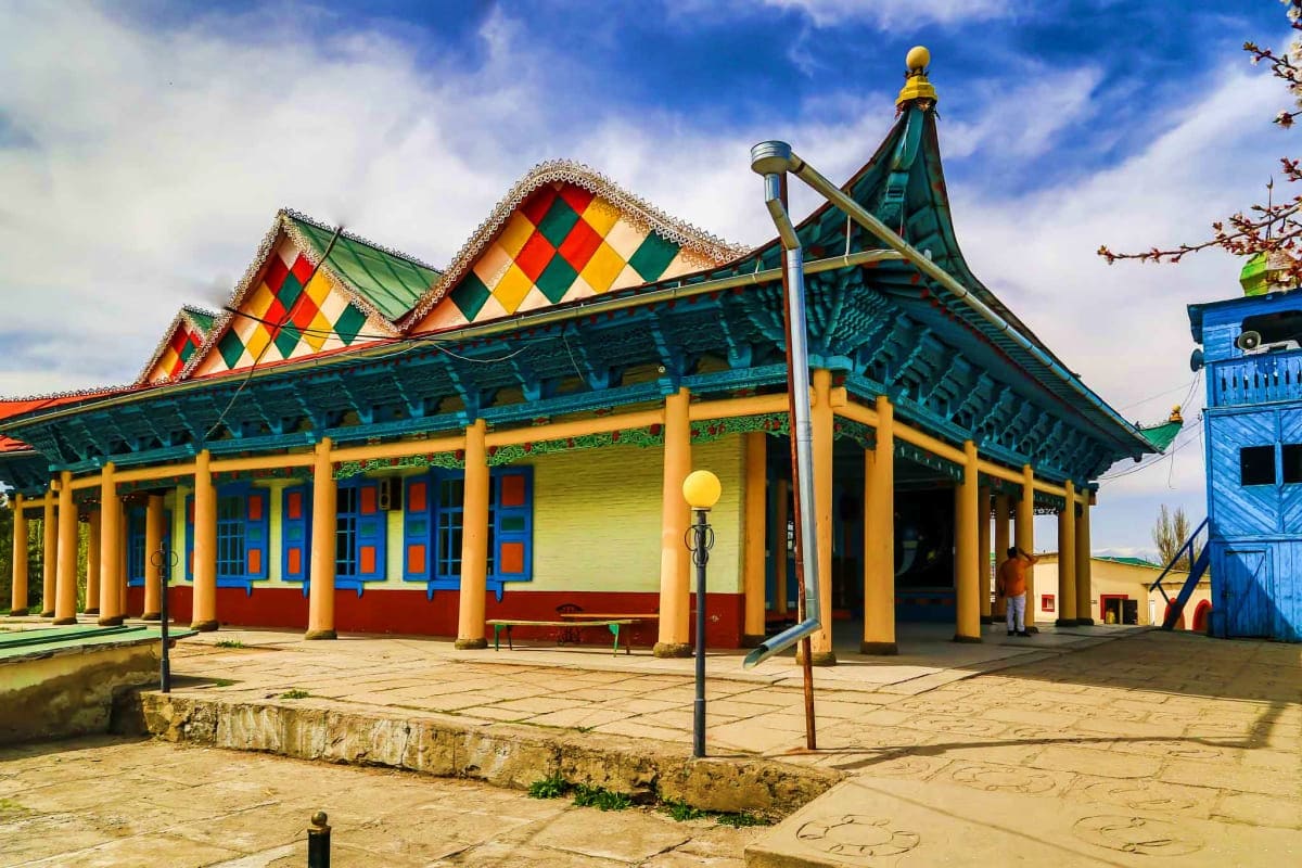 Kyrgyzstan Majestic Landscapes Colorful traditional Kyrgyz building with yellow columns, red diamond-patterned roof, and blue-green trim in Central Asia