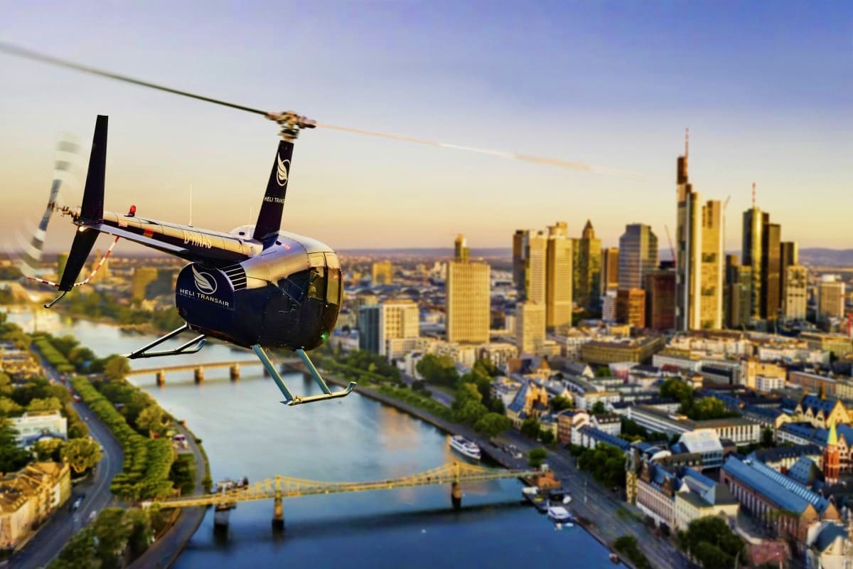 Minsk Super Saver Deal Black and white helicopter flying over Frankfurt skyline with Main River and city bridges visible below at sunset
