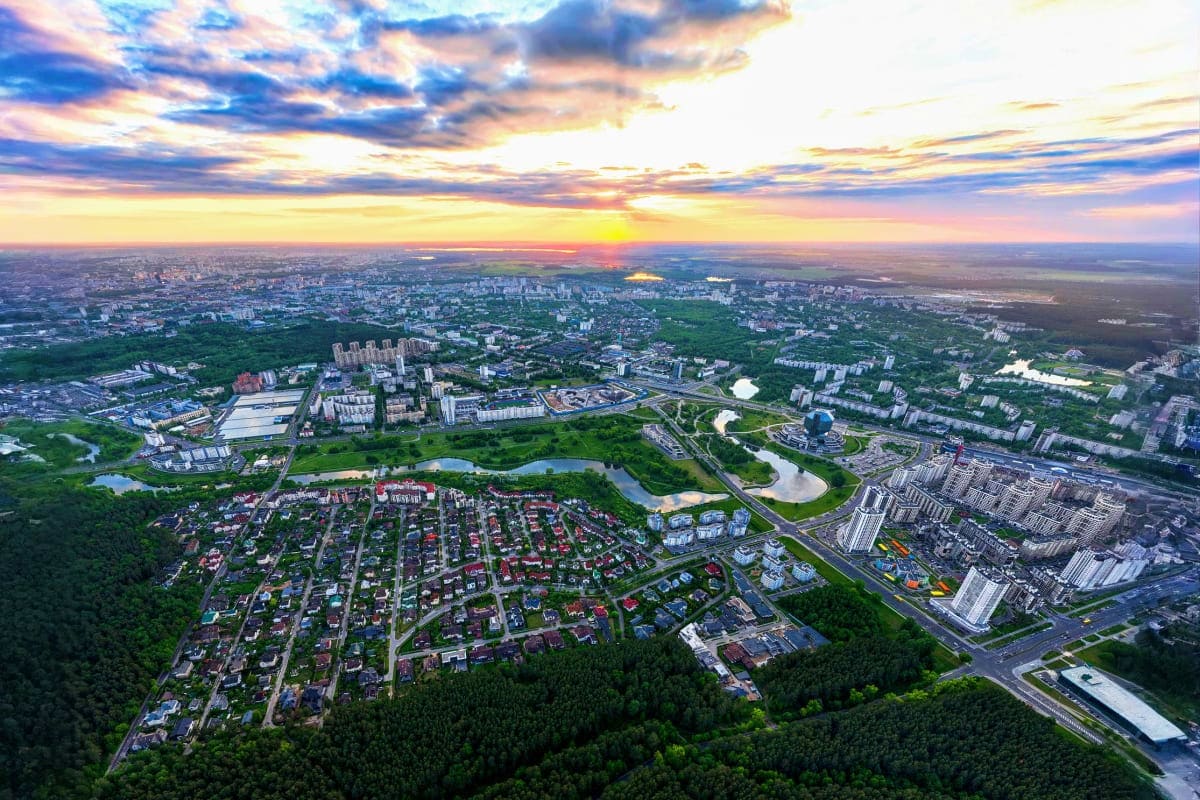 Aerial view of Minsk cityscape at sunset with residential neighborhoods, green parks, rivers, and modern buildings stretching