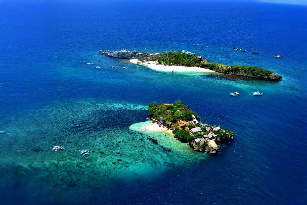 Aerial view of two small tropical islands with white sand beaches, turquoise water, and anchored boats in the Philippines