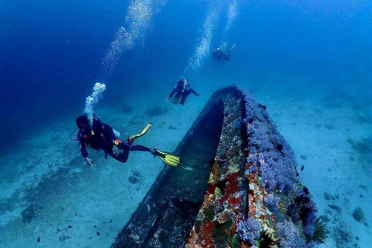 Scuba divers exploring a sunken shipwreck covered in coral and marine growth on the ocean floor in Puerto Galera