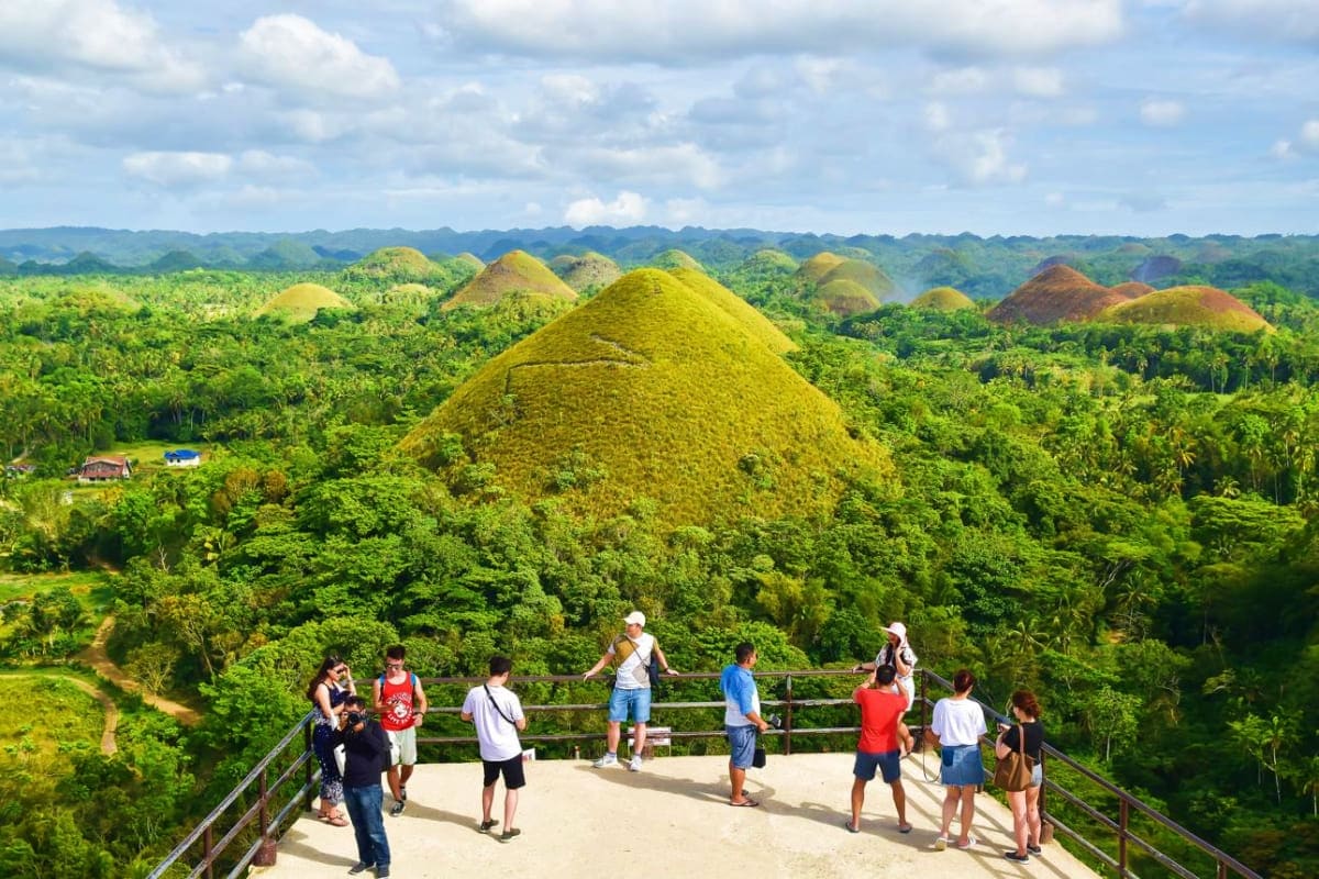 Tourists viewing the Chocolate Hills landscape from an observation platform in Bohol, Philippines, surrounded by lush green f