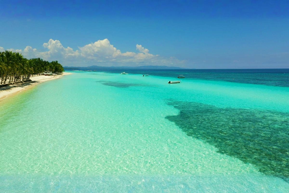 Tropical beach in Bohol with crystal clear turquoise water, white sand, palm trees, and moored boats under blue sky