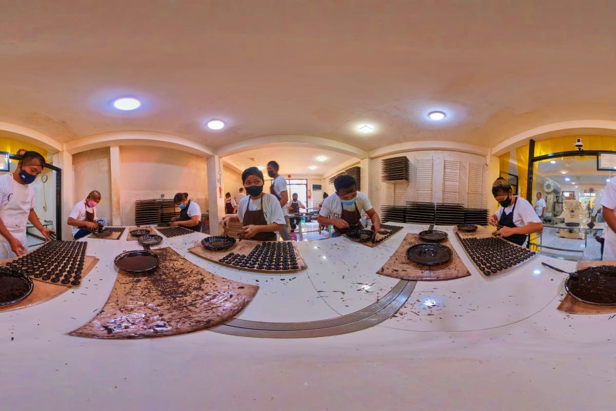 Chocolate-making class with multiple workers piping chocolate onto molds at a confectionery workshop