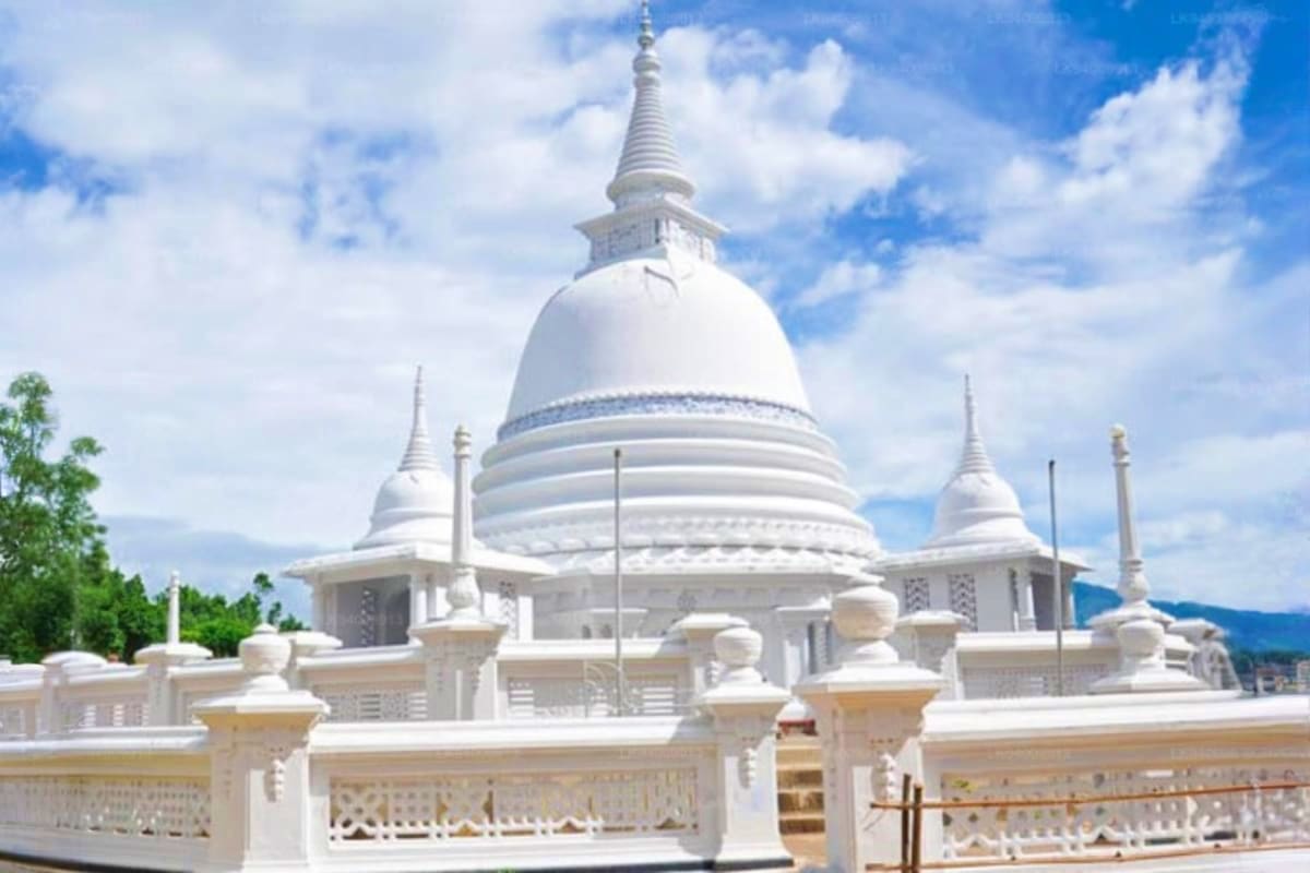 White Buddhist temple with large dome and spires against blue sky with mountains in background
