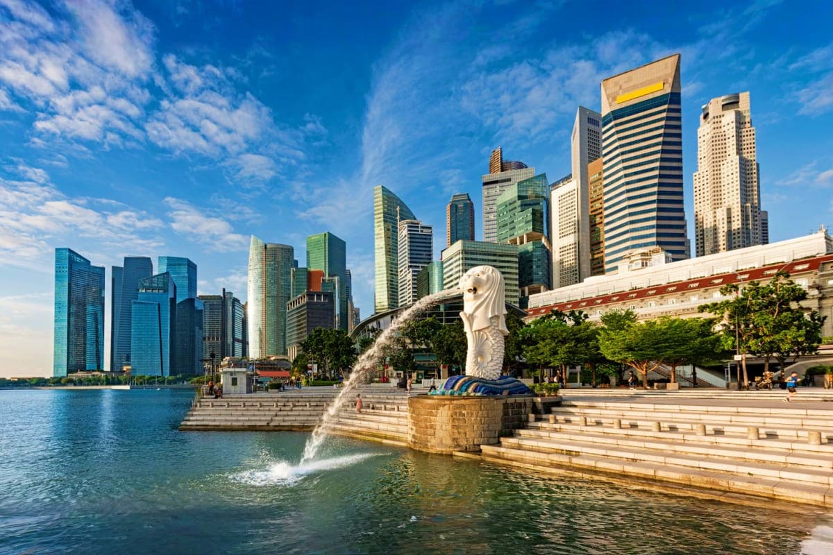 Honeymoon Special Merlion statue spouting water in Marina Bay with Singapore skyline and modern skyscrapers behind, waterfront promenade visibl