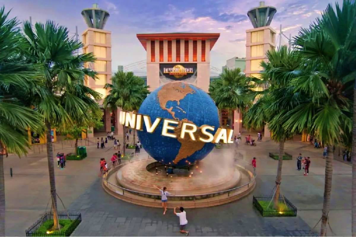 Dream Honeymoon Cruise Vacation Universal Studios theme park entrance with iconic blue globe logo, palm trees, and visitors in the plaza at dusk