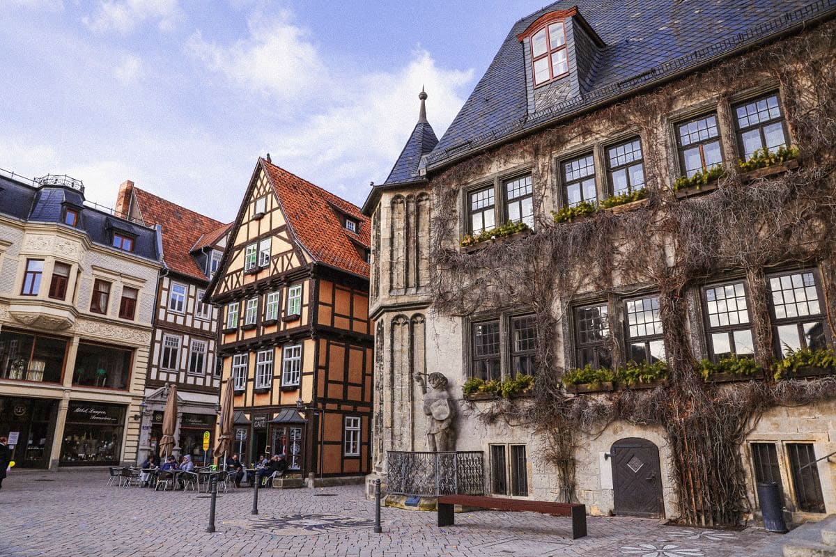 Historic European town square with half-timbered medieval buildings and ivy-covered stone structures under blue sky