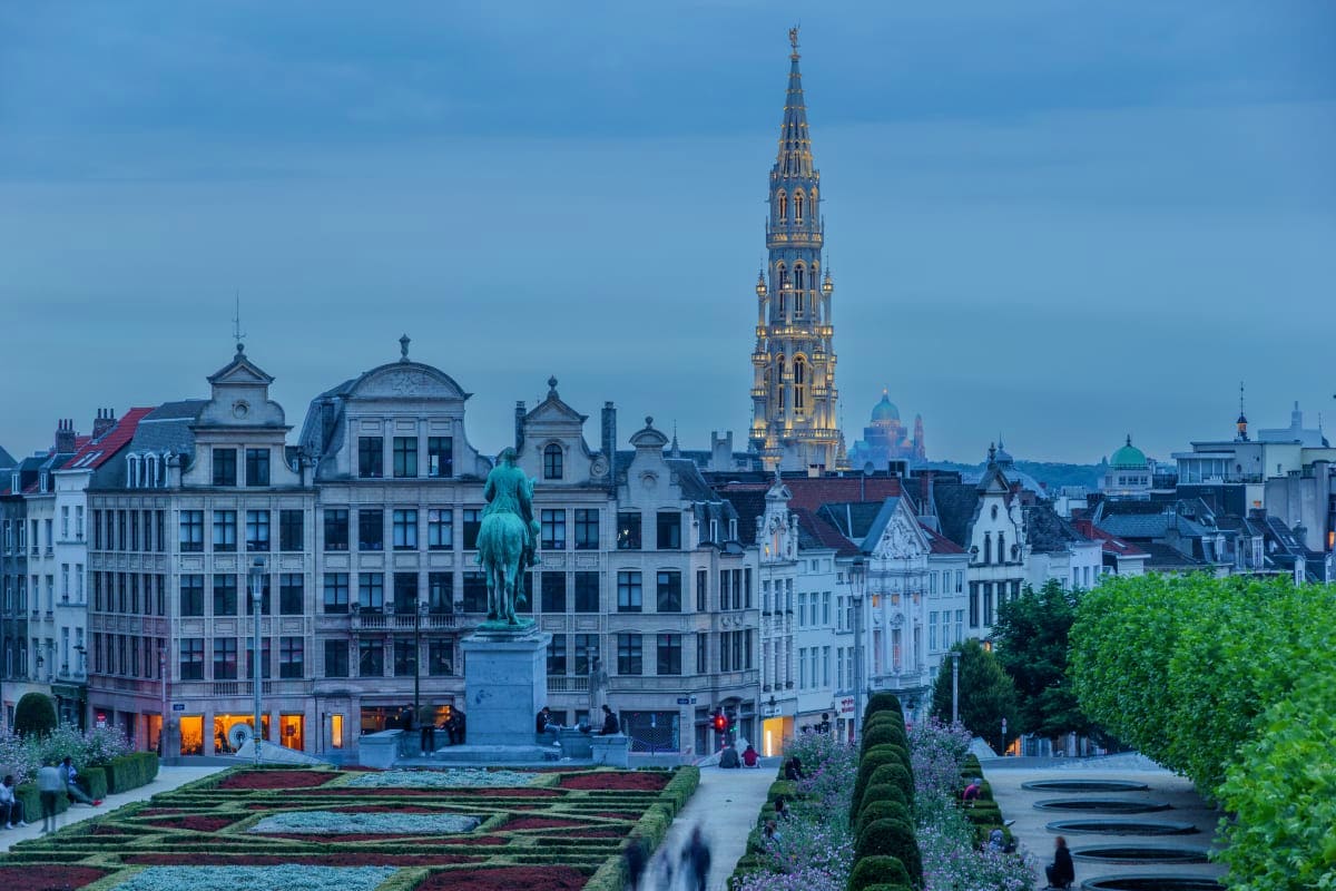 Charming Cities From Brussels to Zurich Brussels cityscape with equestrian statue, Gothic spire cathedral tower, historic buildings, and formal gardens at dusk