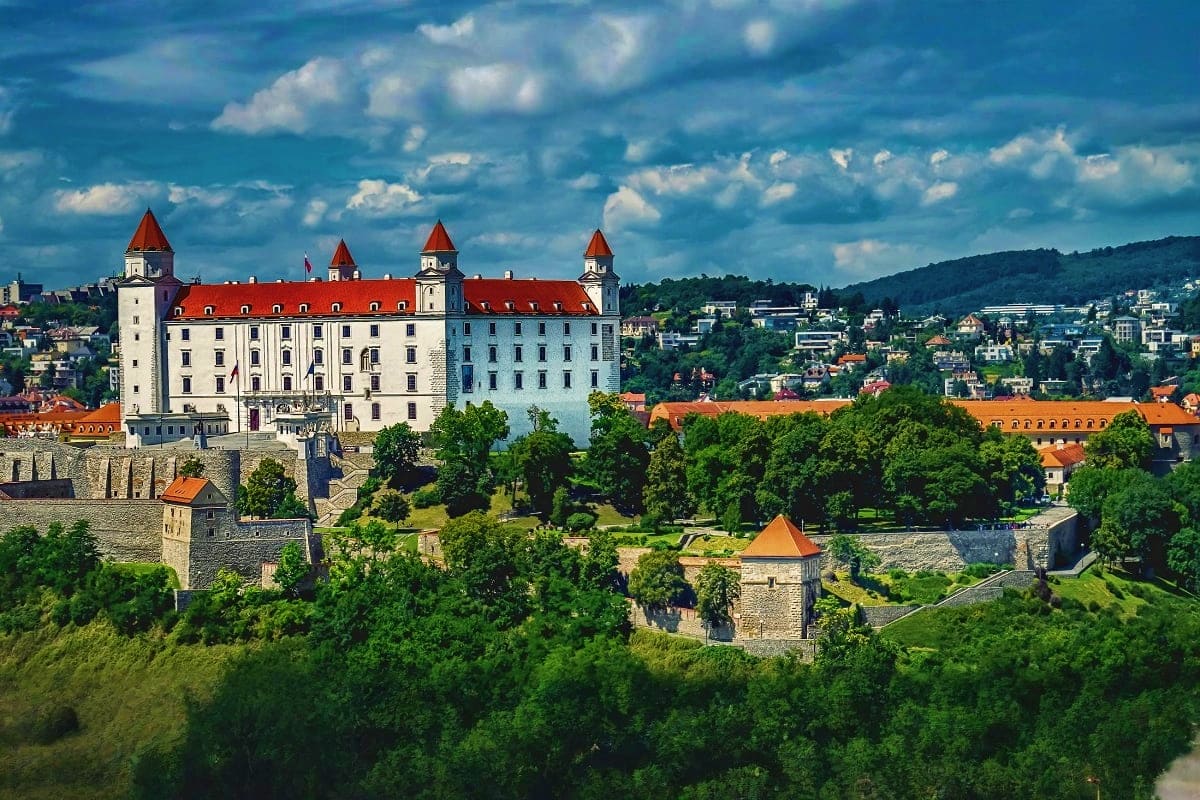 Family tour of Europe From Budapest to Paris Medieval castle with red roof and white walls surrounded by green forests and defensive fortifications on hillside
