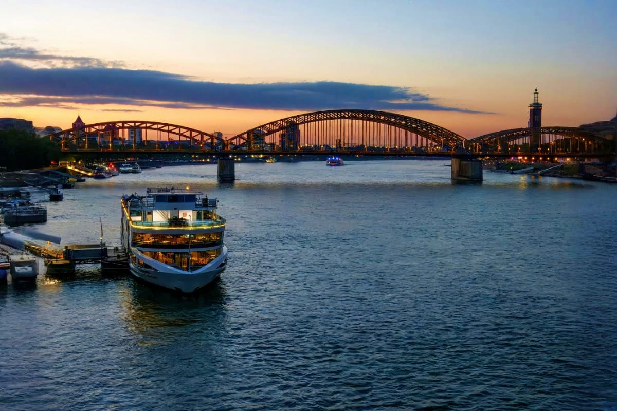 River cruise ship on the Danube at dusk with Iron Bridge illuminated in background, Budapest cityscape visible