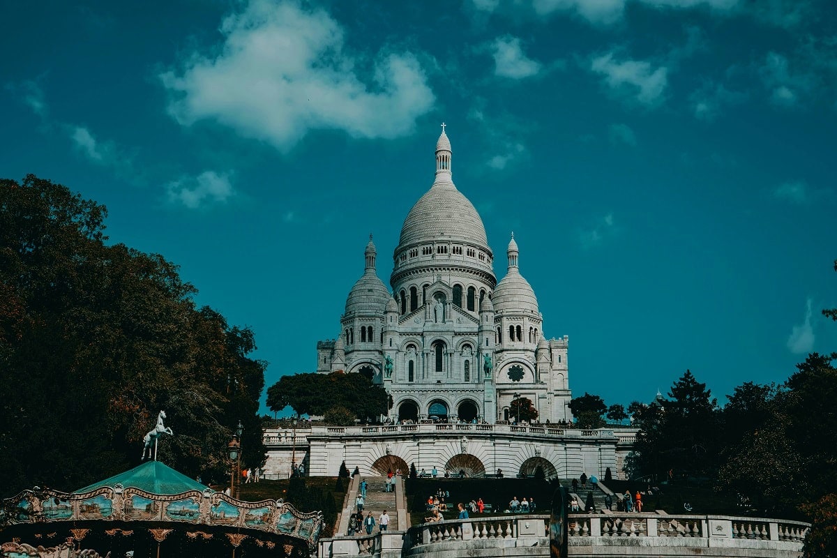 Sacré-Cœur Basilica in Paris with white dome and Romano-Byzantine architecture against bright blue sky with green trees below