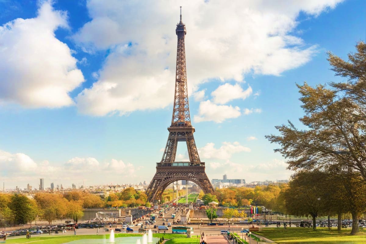 Eiffel Tower in Paris with Trocadéro gardens, autumn trees, and Paris skyline under blue sky with white clouds