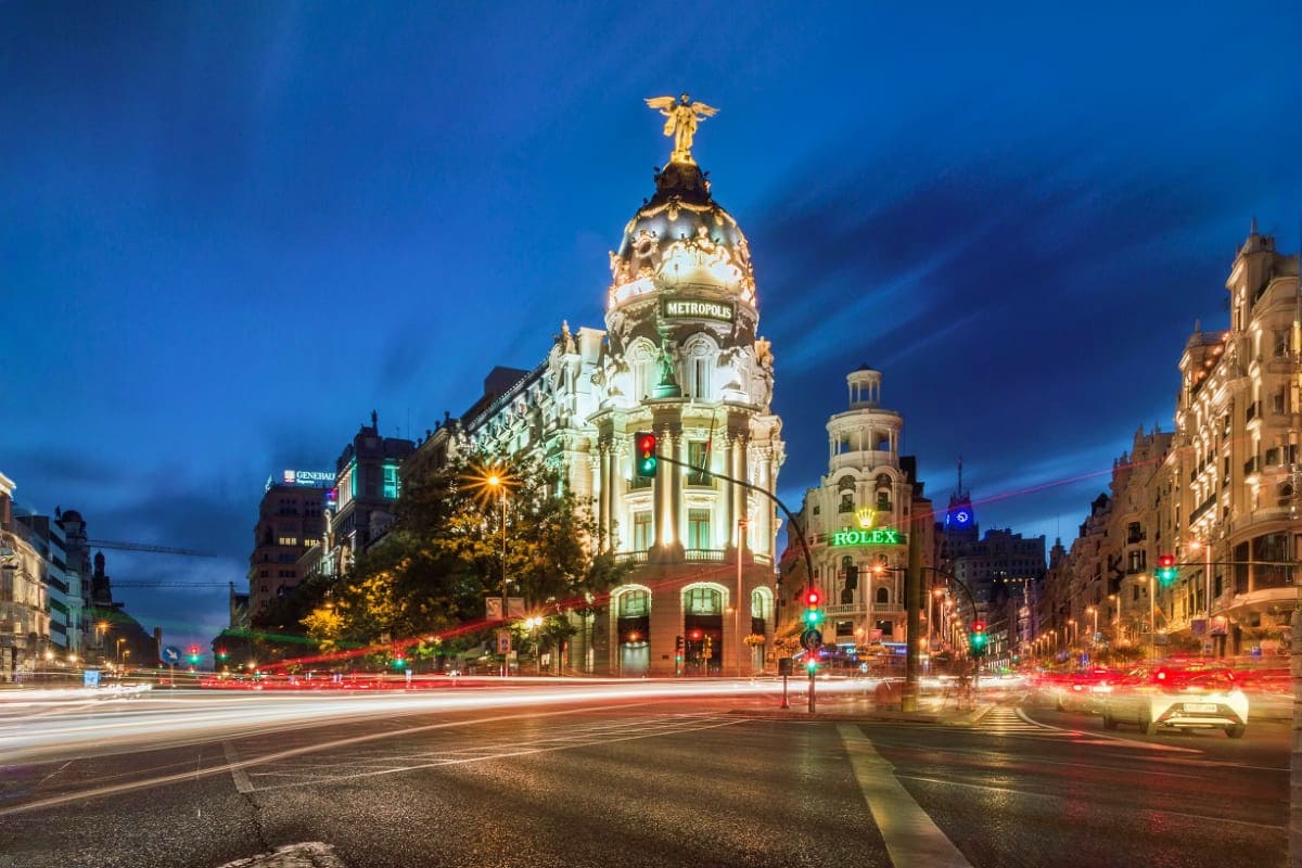 Illuminated Metropolis building at twilight in Madrid with golden angel statue, historic architecture, and light trails from 