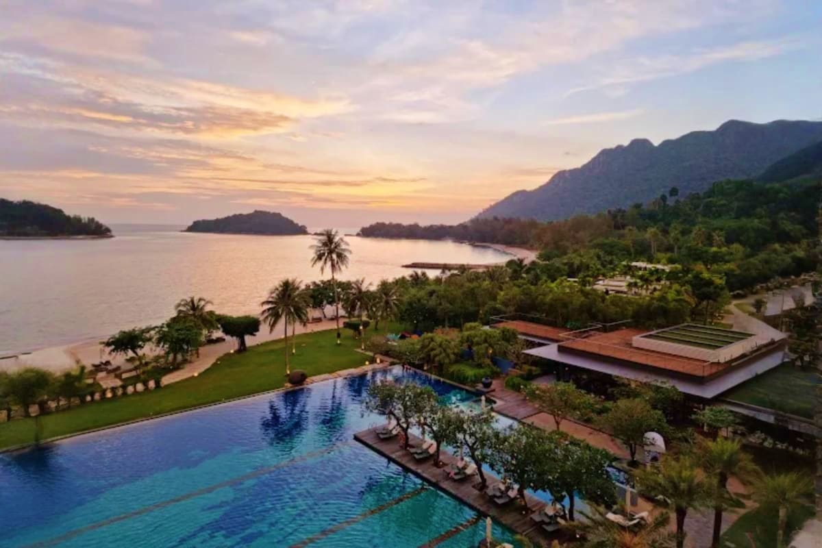 Malaysia Grand Honeymoon Luxury beachfront resort with infinity pool, tropical gardens, and limestone cliffs overlooking calm bay at sunset in Malaysi